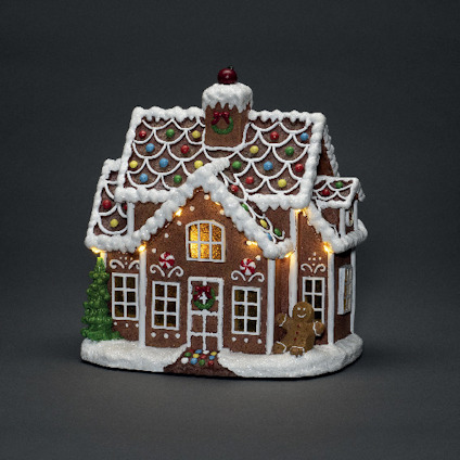 Pepparkakshus dekorerat med glasyr, färgglada godisar, en julgran, en liten pepparkaksgubbe samt lysande ljus.