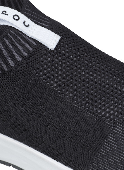 Svart stickad sneaker med vit etikett och synlig textur.