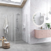 Modernt badrum med glasdusch, rosa kommod, runda speglar och krukväxt. Ljus och stilren design.