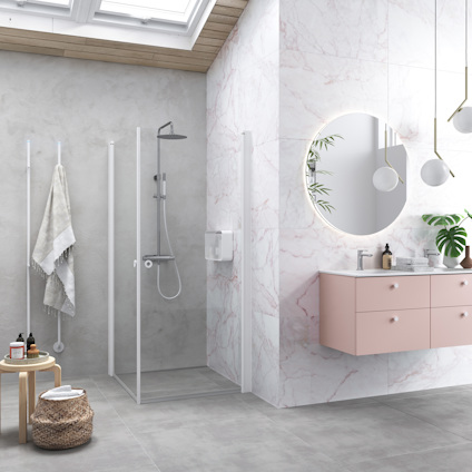 Modernt badrum med glasdusch, rosa kommod, runda speglar och krukväxt. Ljus och stilren design.