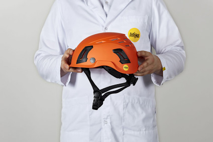 Person i vit labbrock håller orange hjälm med svarta ventiler och säkerhetsrem.