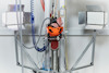 Robotarm med orange hjälm och slangar, omgiven av ljusreflektorer, i industriell miljö.