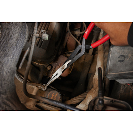 Tång med rött och svart handtag används i en motorrum omgivning för att dra i en rem.