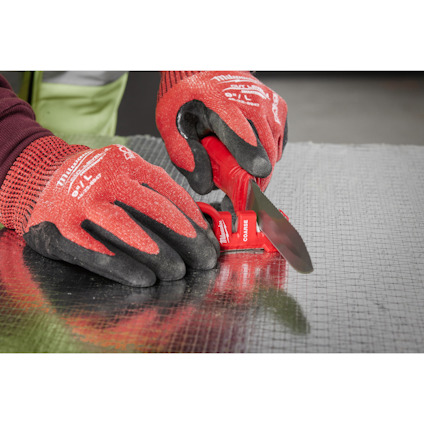 Händer med röda arbetshandskar skär glasfiber med en röd kniv.