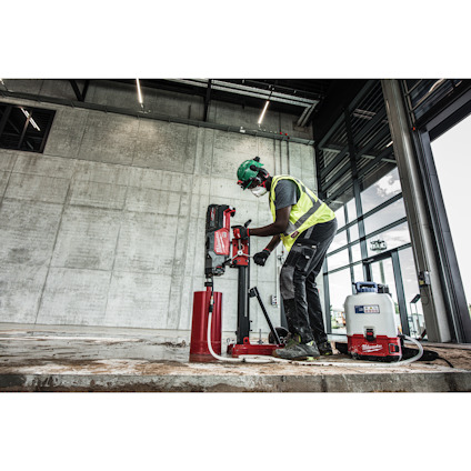 Byggnadsarbetare med skyddsutrustning använder en stor borrmaskin mot en betongvägg i en industriell miljö.