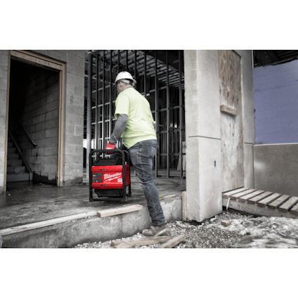 Person in byggekläder och hjälm bär en Milwaukee arbetsradio in på en byggarbetsplats.