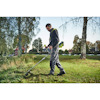 En person använder en grästrimmer av märket RYOBI på en gräsmatta, omgiven av träd och parkmiljö.