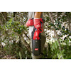 Person wearing red gloves holding a tool in a black holster in a garden setting.
