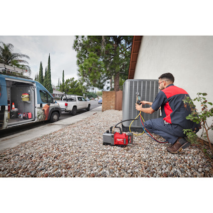 En tekniker arbetar med luftkonditioneringsaggregat utomhus. Flera verktyg syns i bakgrunden.