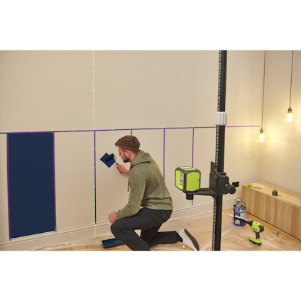 Person målar väggen i blått med hjälp av krysslaser av märket Ryobi och tejp. Verktyg syns på golvet.