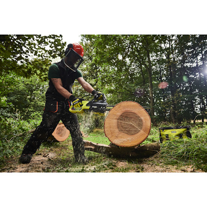 Person med skyddsutrustning sågar en stor trädstock i skog med en kedjesåg av märket Ryobi.
