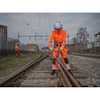 En person i orange arbetskläder använder en maskin på järnvägsspår, med en annan person längre bort.