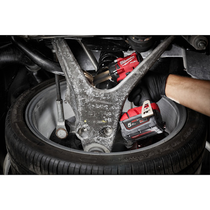 Bilmekaniker justerar skruv med röd och svart borrmaskin under fordon nära däck.
