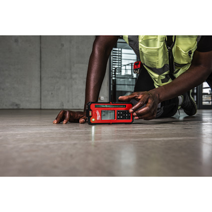 Person i arbetskläder använder en röd lasermätare på ett betonggolv.
