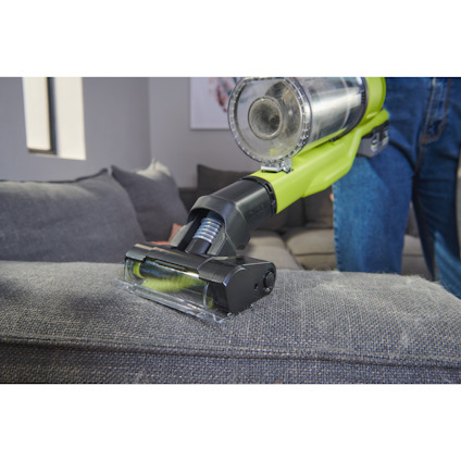 Skaftdammsugare med ett litet motoriserat munstycke i bruk på en grå soffa, användare bär jeans.