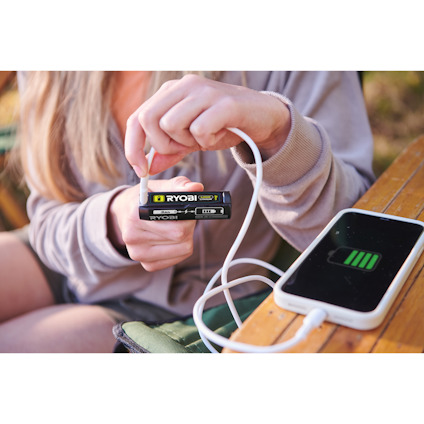 Person som använder ett 4V USB litihum batteri av märket RYOBI för att ladda en smartphone via USB-kabel.