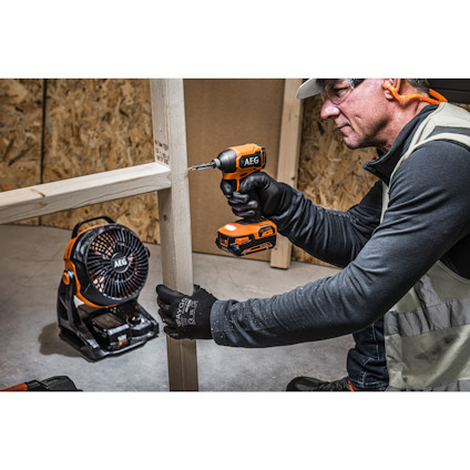 Person med skyddshjälm använder en AEG skruvdragare på en träregel, fläkt syns i bakgrunden.