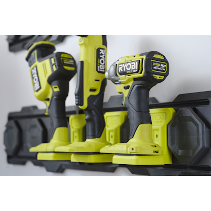 Borrmaskiner av märket Ryobi som hänger på ett svart förvaringsställ på väggen.