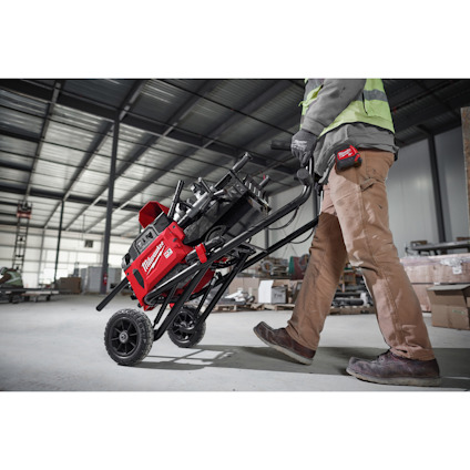 Person drar en röd, portabel sågkärra på en byggarbetsplats.