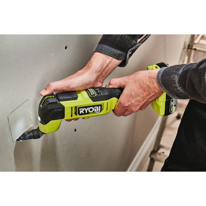 Person använder en grön Ryobi elverktyg för att skära i en vit vägg.