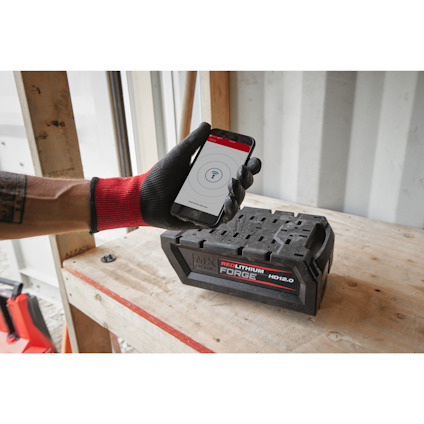 Person med röd och svart handske håller en mobil bredvid ett litiumbatteri märkt "REDLITHIUM FORGE HD12.0".