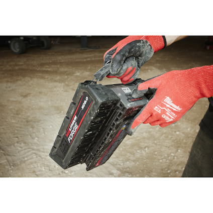 Person som håller ett Milwaukee MX FUEL-batteri, iklädd röda handskar. Batteriet har märkningen "XC60".