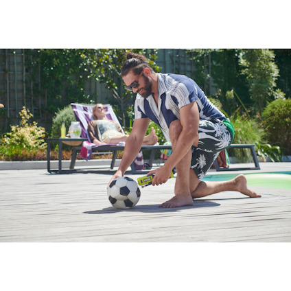 Man använder en volympump av märket Ryobi för att pumpa upp en fotboll på en träaltan nära en solstol.