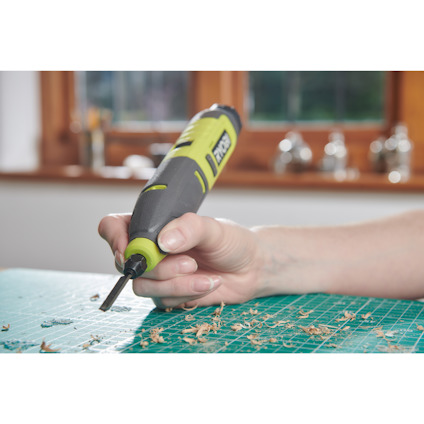 Hand som håller ett grönt batteridrivet stämjärn från Ryobi ovanpå en grön skärmatta.