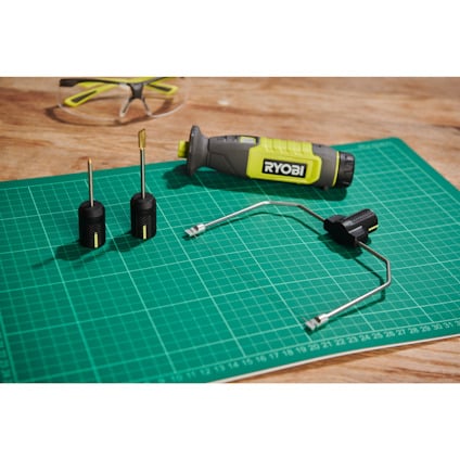 Varmskärare från Ryobi och bits på grönt skärunderlägg med en Ryobi skyddsglasögon i bakgrunden.