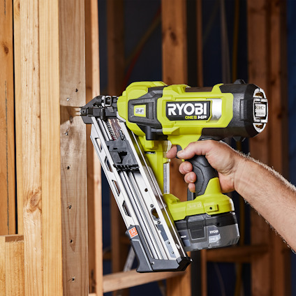 En person använder en grön Ryobi One+ stavspikpistol mot en träram.