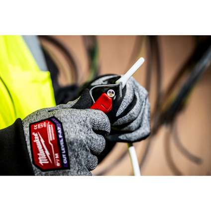 En person med handskar skär en vit kabel med en röd kabelskalare i en arbetsmiljö.