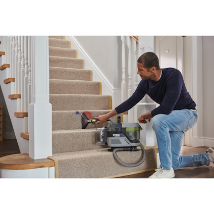 Man använder en liten dammsugare för att rengöra en trappa med beige matta.