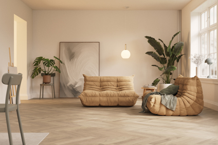 Ljust vardagsrum med beige soffor, stora växter och en rund taklampa. Ljust träfärgat golv och stora fönster.