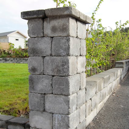 Grå stenmur och pelare omgivna av gräsmatta och växtlighet i bakgrunden.