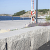 Grå stenmurar vid en vattenkant med en livboj och stege i bakgrunden.