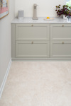 Pale beige floor tiles in a kitchen with light green cabinetry and a countertop with a lemon and plant.