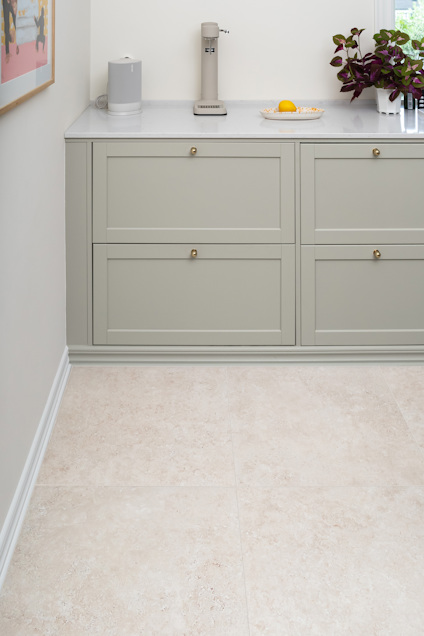 Pale beige floor tiles in a kitchen with light green cabinetry and a countertop with a lemon and plant.