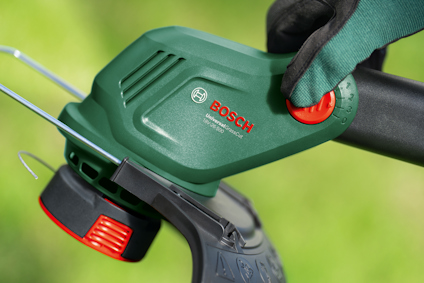 Grön Bosch trimmer, hand i trädgårdshandske justerar hastigheten med ett rött vred.