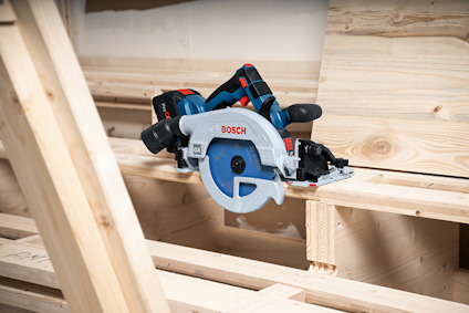 Cirkelsåg märkt "Bosch" placerad på en träkonstruktion, omgiven av träplankor och byggmaterial.