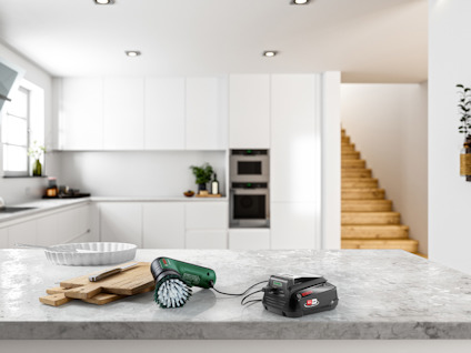 Köksmiljö med laddare, grön elektrisk borste och bakplåt på en stenbänk.