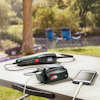 Borrmaskin och smartphone laddas med ett batteripaket på ett campingbord vid en sjö.