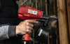 Person som håller en röd spikpistol med märket "Senco", fäster material mot trästödmur.