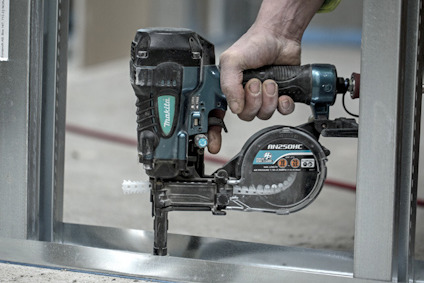 Hand använder en blå och svart kapsåg för metall med etikett "Makita" som skär i en metallram.