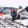 En hand håller en verktygspistol ovanför armeringsstänger på en byggarbetsplats i oskärpa.