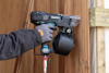 Person i arbetskläder använder en Makita spikpistol mot en trävägg.