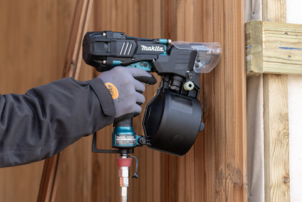 Person i arbetskläder använder en Makita spikpistol mot en trävägg.