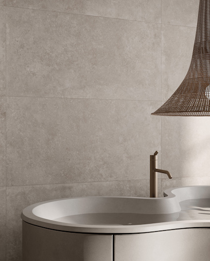 Vägg med stora, beige keramiska plattor bakom ett modernt oval badkar och en minimalistisk kran.