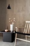 Trästol och bord med svart skiva, vas med bomullsblommor, hängande svart lampa, beige ribbad vägg.