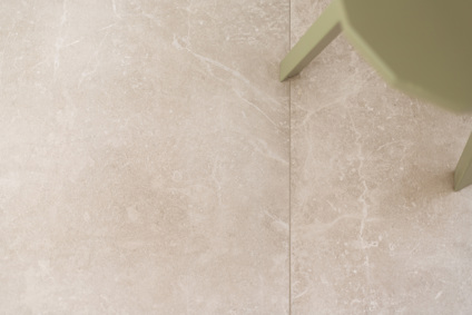 Beige kakelgolv med svaga marmoreringar och ett hörn av en mörkgrön möbel.