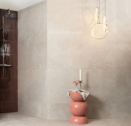 Modernt badrum med stora beige kakelplattor, dusch med mörka paneler, rosa piedestal och hängande lampa.